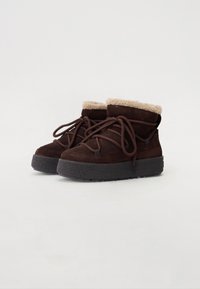 Bottes mi-hautes en suede marron avec une douce doublure en fourrure crème, un laçage robuste et une épaisse semelle noire texturée.