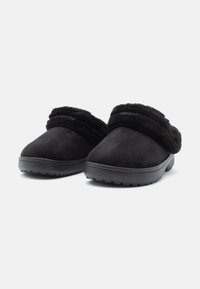 Egy pár fekete slip-on papucs puha műszőrme béléssel és tartós, textúrázott talppal, egymás mellett helyezve fehér háttér előtt.