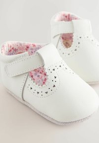 Chaussures pour bébé en cuir blanc avec un design à lanière T, des détails perforés et une doublure rose à motif floral. Semelle souple pour un meilleur confort.