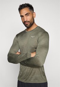 Olivno zeleni shirt z dolgimi rokavi iz teksturiranega materiala, ki ima okroglo ovratnik in majhen bel logotip na prsih.