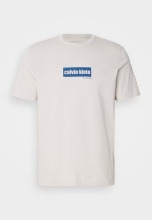 Bela bombažna majica s kratkimi rokavi z modrim pravokotnim logotipom, na katerem sta napisana "calvin klein" in "new york city" z belim besedilom spredaj. Klasičen kroj.