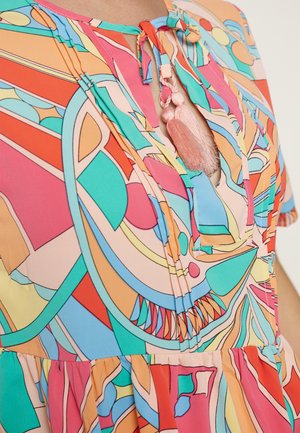 Farverig bluse med mønster, der indeholder abstrakte former, med nøglehulshalsudskæring og dekorative lyserøde kvastestropper.