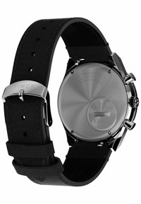 Montre Timex avec un boîtier argenté poli, un bracelet en cuir noir minimaliste et un fond en acier inoxydable avec des détails gravés.
