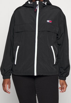 Veste à capuche noire avec fermeture éclair blanche et fermetures éclair des poches, poignets élastiques, et un petit logo Tommy Jeans sur la poitrine.