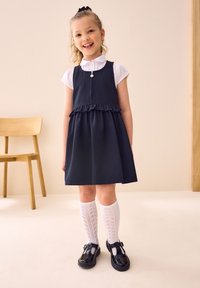 Tumesinine kleit volangikujundusega, mida kantakse valge kraega särgiga, valgete põlvikutega ja mustade läikiva nahaga kingadega.