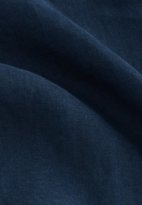 Tessuto blu navy con superficie liscia e strutturata, che mostra pieghe morbide e una lucentezza sottile. Il materiale sembra leggero e traspirante.