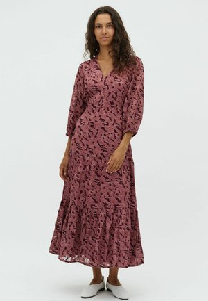 Maxiklänning i mjuk rosa tyg med abstrakta mörka mönster, V-ringning, 3/4 puffärmar och volangkant. Bärs med vita ballerinaskor.