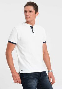 Hvid kortærmet polo shirt med en marineblå krave og tre-knaplukning. Struktureret stof med en tætsiddende pasform og kontrasterende ærmeaccenter.