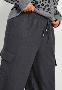 Grijze cargo-broek met een elastische tailleband en trekkoord. Beschikt over een zijzak en een gestructureerde stof met een zachte, iets gestructureerde uitstraling.