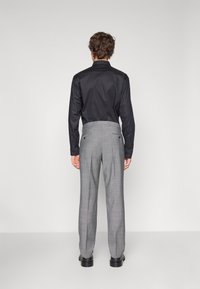 Schwarzes Langarmhemd kombiniert mit hellgrauen karierten Hosen. Die Hosen verfügen über zwei Gesäßtaschen, und die Schuhe sind schwarz mit einer glatten Oberfläche.