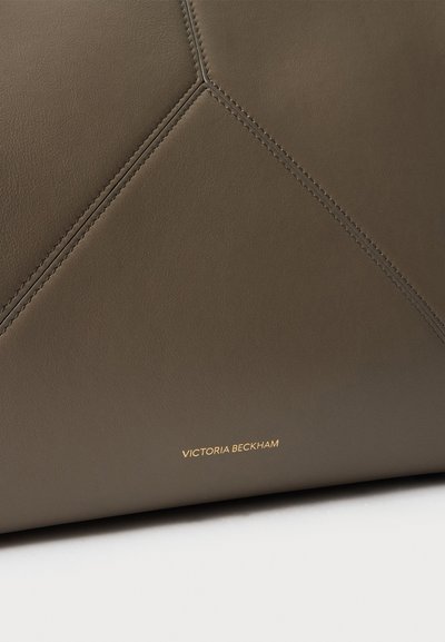 Gros plan d'un sac à main en cuir marron avec motif losange cousu et petit logo doré Victoria Beckham sur la partie inférieure.