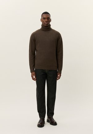 Suéter marrón de cuello alto con relieve, silueta ajustada, combinado con pantalones de mezclilla oscuros y botas de cuero marrón. Fondo neutro.