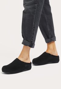 Black slip-on clogs with a soft fur lining at the collar and a rounded toe shape, set against gray cuffed denim pants.