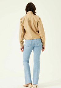 Beige džínsová bunda s límcem a knoflíkovými manžetami, doplněná světle modrými zvonovými džíny. Hladká tkanina, zkrácený design, minimální detaily.