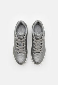 Graue Sportschuhe mit einer perforierten Oberfläche, runden Zehen und passenden Schnürsenkeln, ausgestattet mit einer gepolsterten Sohle und dem Skechers-Logo an der Seite.