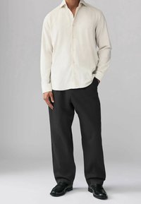 Camisa button-up color beige claro, pantalones anchos negros, zapatos negros; tejido suave, ajuste entallado, mangas largas, ligero brillo en la camisa.