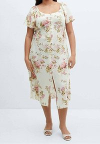 Robe midi florale en crème, avec des manches courtes en volants, un devant à boutons et une fente à l'avant. Tissu doux avec un motif floral rose et vert.