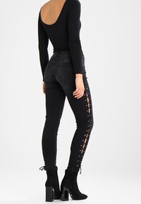 Svarta skinny jeans med snörning på sidan, i en blandning av bomull, och en figurnära passform. Kombineras med svarta klackade ankelstövlar.