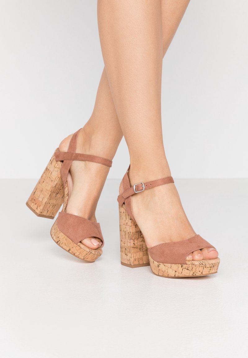 Růžové semišové platformové sandály s tlustým korkovým podpatkem. Mají design s odhalenými prsty a řemínek kolem kotníku se stříbrnou sponou.