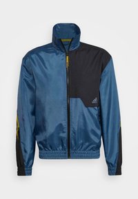 Blaue und schwarze Zip-Jacke mit hohem Kragen, elastischem Saum und elastischen Ärmelbündchen. Verfügt über eine strukturierte Tasche und kontrastierende gelbe Akzente.