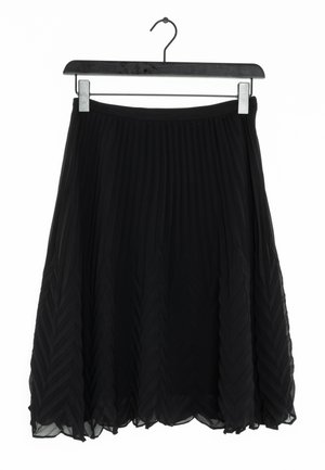 Falda negra plisada con un diseño fluido y en capas. Confeccionada en una tela ligera con un patrón de grecas, colgando de un simple gancho de metal.