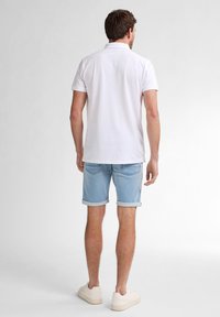 Polo shirt bianco a maniche corte, vestibilità casual, abbinato a pantaloni shorts in denim azzurro chiaro arrotolati all'orlo, indossato con sneakers crema.