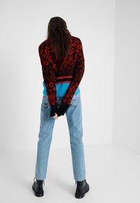 Dzianinowy sweter z czarno-czerwonym leopardowym wzorem, niebieskim prążkowanym akcentem, w zestawieniu z jasnoniebieskimi dżinsami i czarnymi botkami na kostkę.