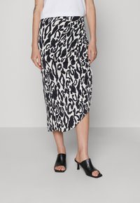Jupe midi en imprimé léopard noir et blanc, avec des détails de ruching sur le côté et un ourlet asymétrique. Associée à des mules ouvertes noires.