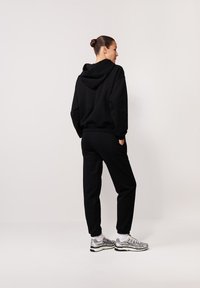 Czarna bluza z kapturem i dresy wykonane z miękkiego materiału. Bluza ma dużą kieszeń i sznurek do regulacji, z ściągaczami na mankietach. Połącz z srebrnymi sneakersami.