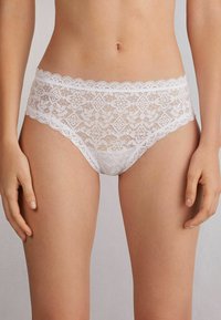 Witte kanten bikini-stijl ondergoed met bloempatronen en golvende randen, met een doorschijnende textuur en een gedetailleerd ontwerp.