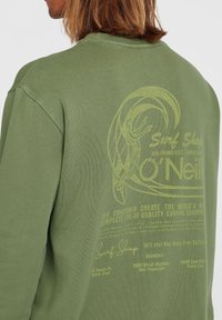 Groene longsleeve t-shirt met een vintage-geïnspireerde gele grafische print op de achterkant, met de merknaam en details van de surfshop. Zachte stof.