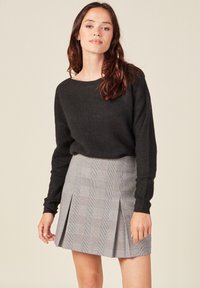 Schwarzer Strickpullover mit langen Ärmeln, kombiniert mit einem grauen Karo-gefalteten Rock, der ein kariertes Muster und Seiteneinfaltungen aufweist.