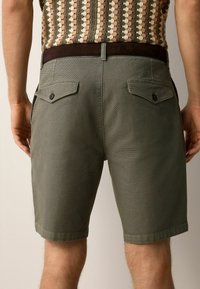 Grønne vævede shorts med en tætsiddende talje, to baglommer og knapdetaljer, med en kort benlængde. Struktureret stof.