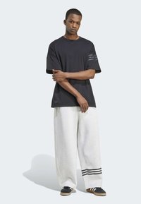 Black t-shirt with short sleeves and three horizontal stripes on one arm, paired with light grey wide-leg sweatpants featuring dark stripes.