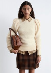 Cream puff-sleeve sweater with a beige plaid shirt underneath, paired with a brown plaid skirt and a brown leather handbag.