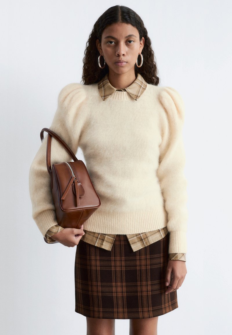 Cream puff-sleeve sweater with a beige plaid shirt underneath, paired with a brown plaid skirt and a brown leather handbag.