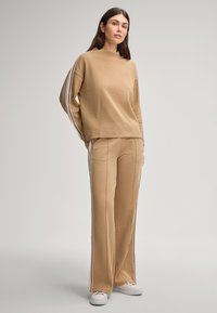 Felpa beige e pantaloni abbinati realizzati in morbido tessuto. La felpa ha maniche lunghe con strisce a contrasto; i pantaloni presentano strisce laterali.