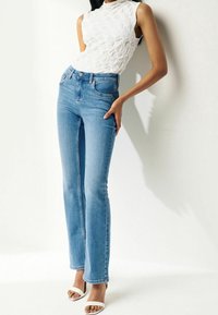 Jeans de mezclilla claros con corte acampanado y cintura alta, con bolsillos frontales y detalles de costura. Combinados con una blusa sin mangas blanca texturizada.