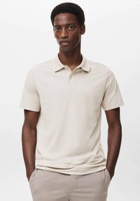 Camisa polo beige de manga corta, con un cuello estrecho y una tapeta de tres botones. Textura suave, corte casual, combinada con pantalones color beige claro.