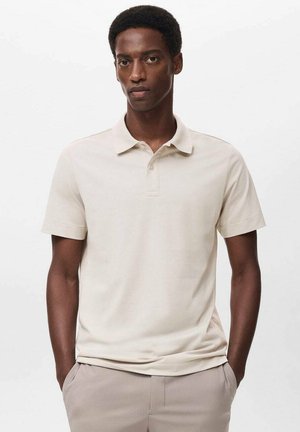Camisa polo beige de manga corta, con un cuello estrecho y una tapeta de tres botones. Textura suave, corte casual, combinada con pantalones color beige claro.