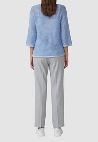 Helle blaue kurzärmlige Strickoberteil mit strukturiertem offenen Muster, kombiniert mit grauen maßgeschneiderten Hosen und weißen Sneakern.