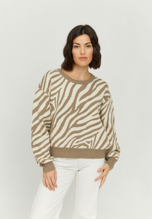 Knitted sweater featuring a beige and white zebra pattern, loose fit, round neck, and ribbed cuffs and hem. Paired with white trousers.