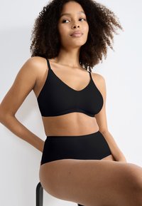 Bralette noire avec bretelles réglables et une texture lisse, associé à des sous-vêtements noirs taille haute. Design minimaliste, sans motifs visibles.