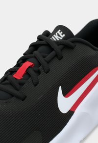 Μαύρο αθλητικό παπούτσι με υφή στην επάνω πλευρά, λευκό και κόκκινο λογότυπο Nike, κόκκινο θηλάκι για τα κορδόνια και αντίθετη λευκή σόλα. Κορδόνια σε πρότυπο σταυρωμένου δεσίματος.