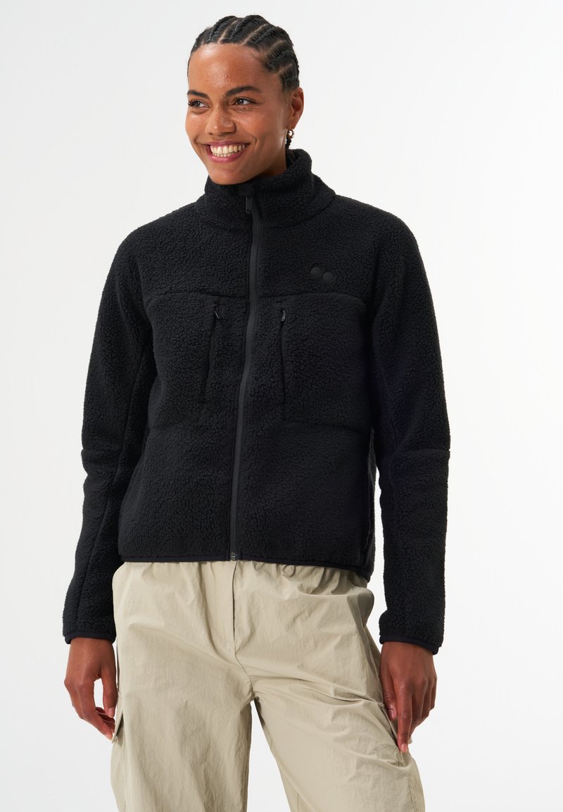 Schwarze Fleecejacke mit hohem Kragen, Reißverschluss und zwei Brusttaschen. Sie besteht aus einem strukturierten, weichen Material und hat eng anliegende Ärmel.