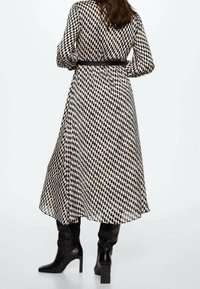 Vestido largo, con estampado en blanco y negro, con cintura entallada y falda fluida. Combinado con botas de cuero negro hasta la rodilla y un cinturón negro.