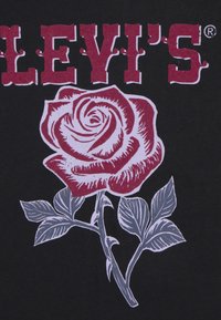 La camiseta negra presenta "LEVI'S" en rojo, con un gráfico detallado de una rosa bicolor en rojo y gris, acompañada de hojas estilizadas en verde.