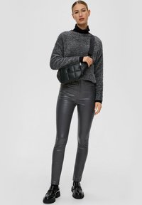 Suéter gris texturizado con acentos negros, pantalones ajustados de imitación de cuero gris brillante de cintura alta, y un bolso de hombro acolchado negro. Zapatos negros gruesos.
