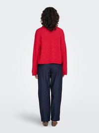 Pull rouge texturé à coupe décontractée, longueur courte et épaules tombantes, assorti à un pantalon bleu marine à jambes larges et des chaussures marron.
