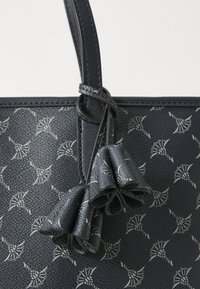 Navy handbag featuring a patterned design and a bow-like detail on the strap, showcasing a stylish and sophisticated look.